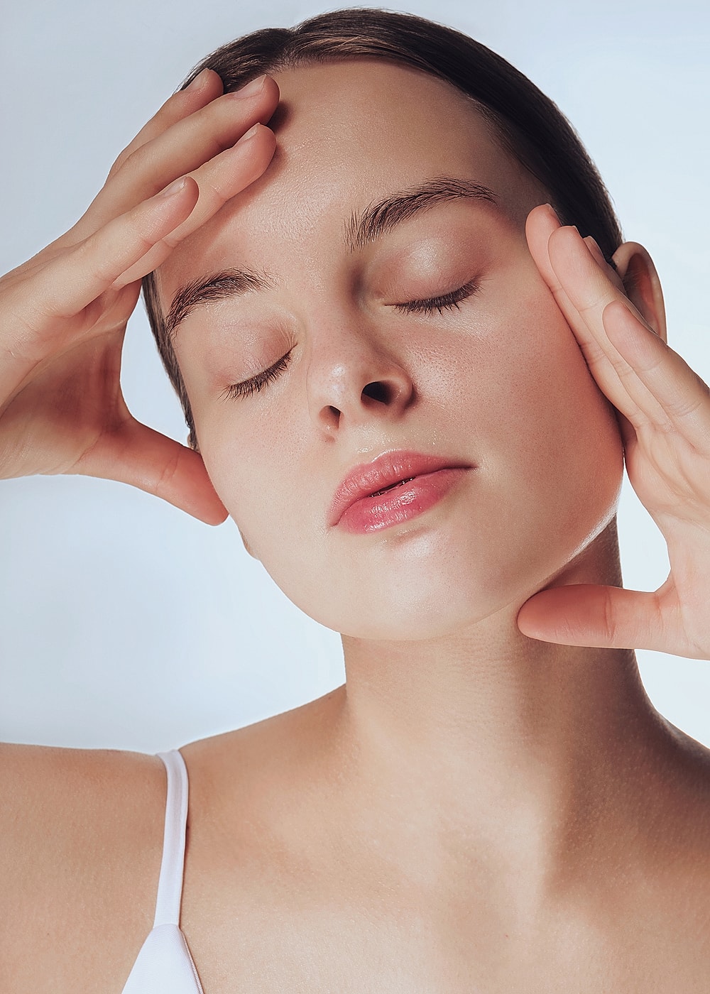 Woman with closed eyes, gently touching her face.