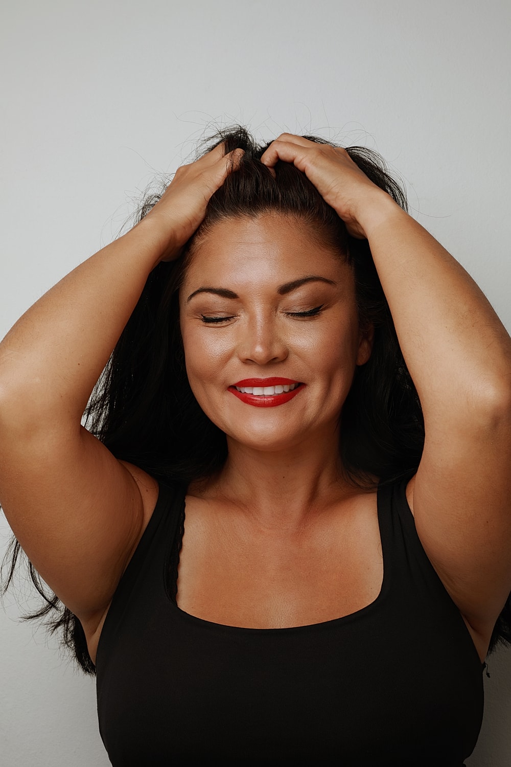 Woman smiling with hands in hair, eyes closed.
