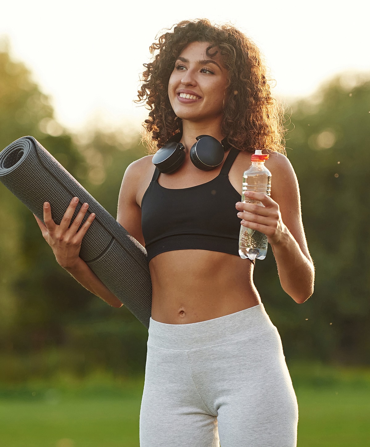 Smiling woman holding yoga mat and water bottle.