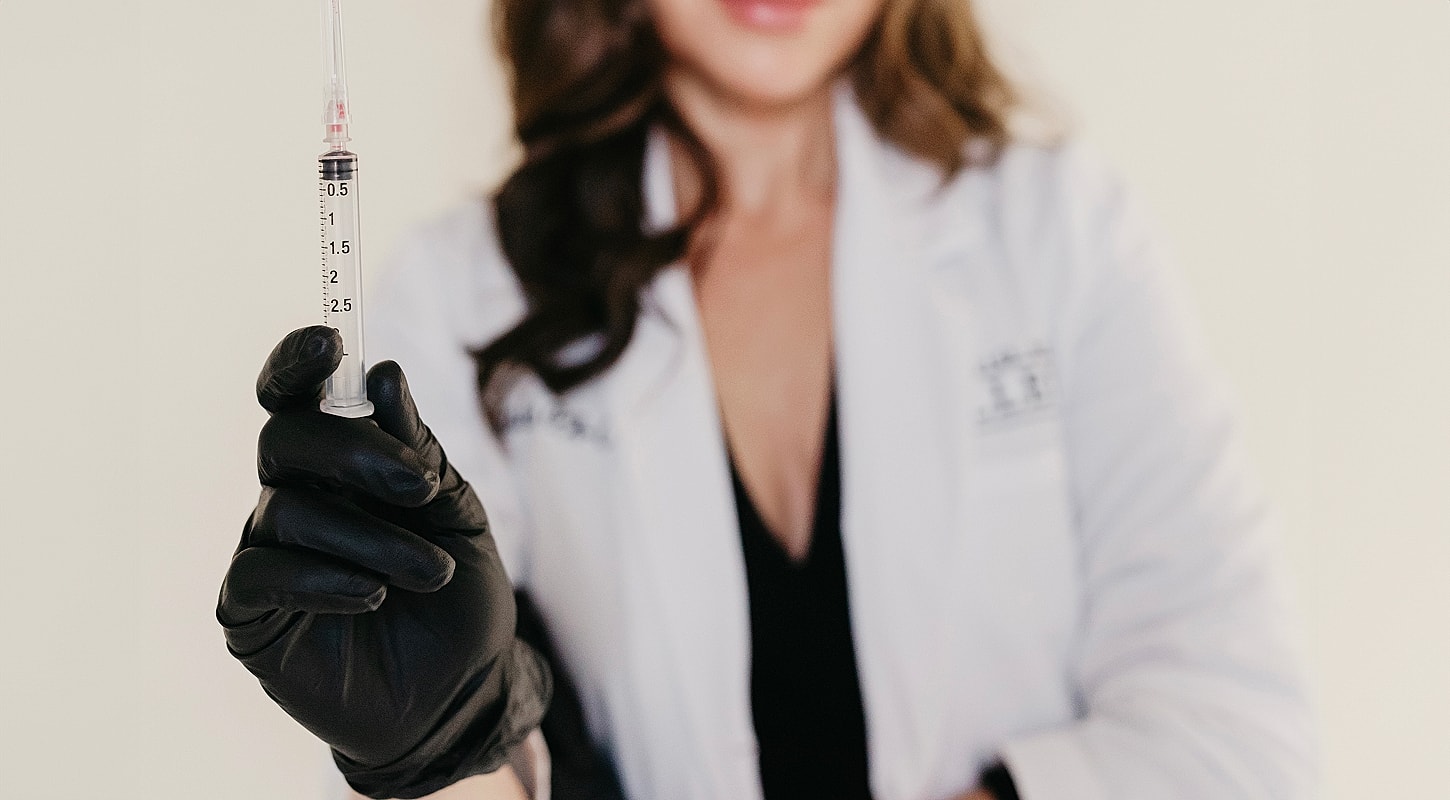 Person in lab coat holding a syringe.